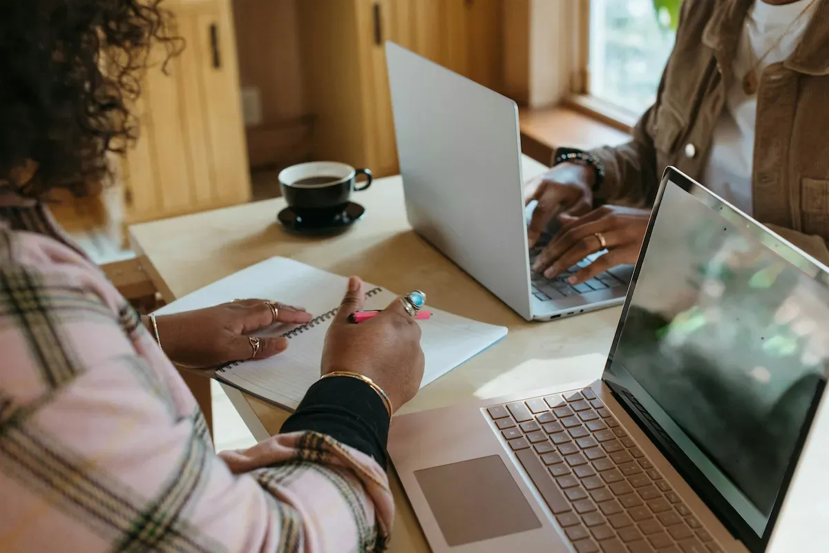 Two women at a table working on their laptops